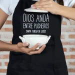 Delantal negro con la frase “Dios anda entre pucheros”, producto solidario de Have a God Time