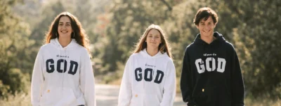 Jóvenes caminando al aire libre con sudaderas cristianas con el mensaje “All you need is God”