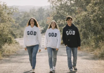Jóvenes caminando al aire libre con sudaderas cristianas con el mensaje “All you need is God”